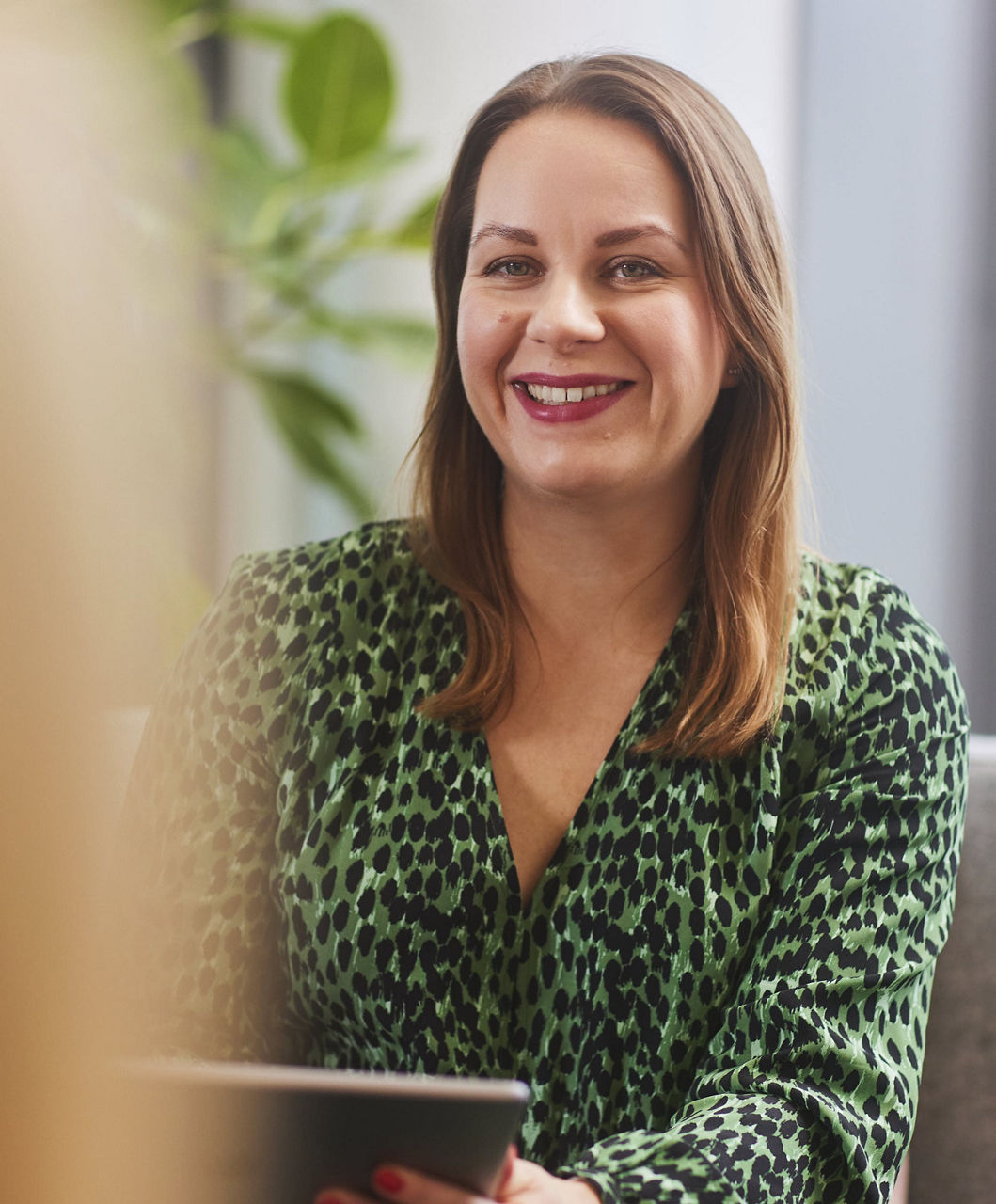 Woman smiling sitting down and holding a tablet
