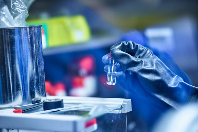 Picture of a hand wearing a glove and picking up a pipet.