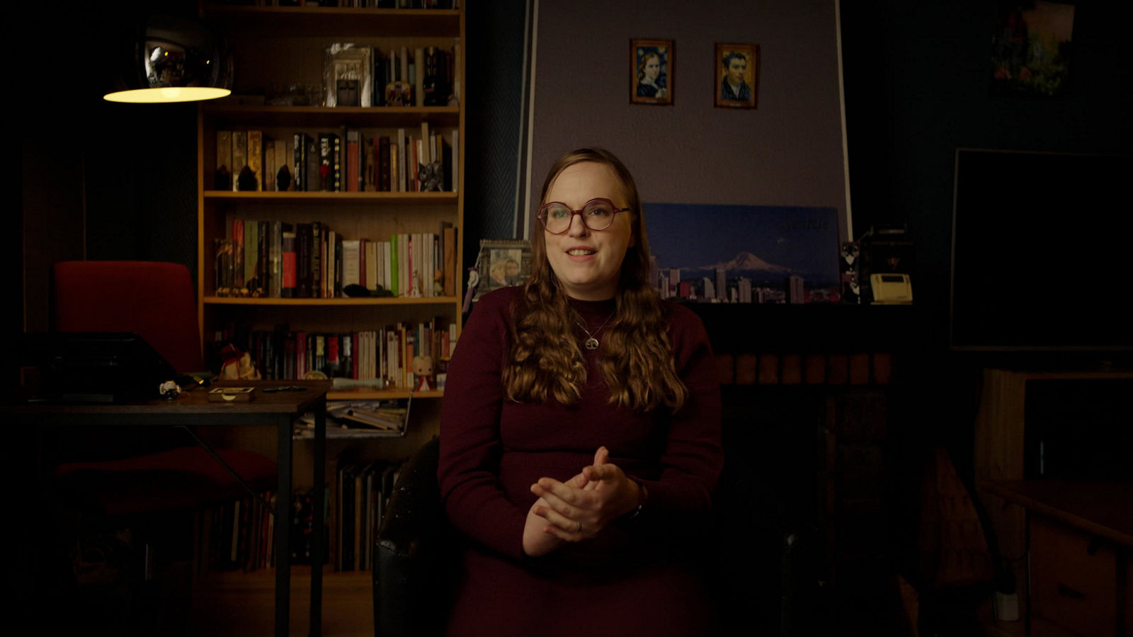 Migraine patient and advocate Morgane is wearing a maroon dress, seated in a black chair in her home office