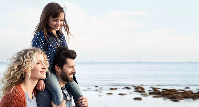 A young family of three walking by the ocean.